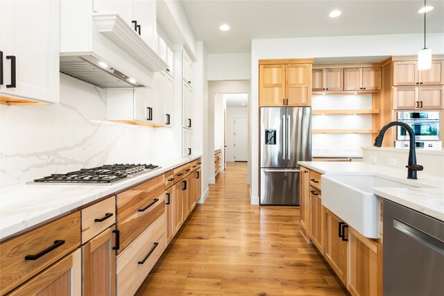 kitchen with custom exhaust hood, white cabinets, appliances with stainless steel finishes, light hardwood / wood-style flooring, and sink