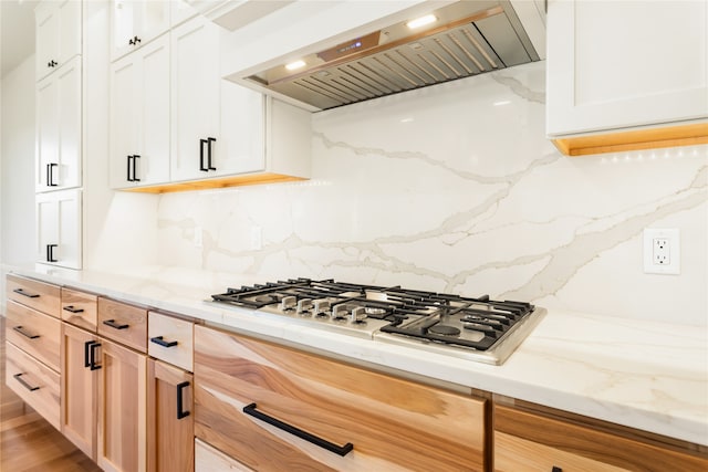 kitchen with white cabinets, tasteful backsplash, wood-type flooring, stainless steel gas cooktop, and wall chimney exhaust hood