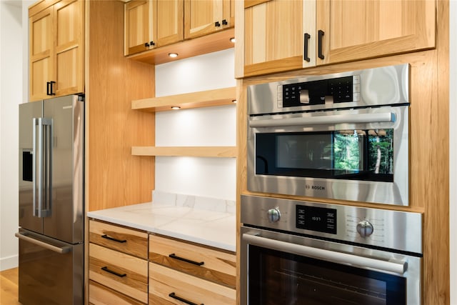 kitchen with light stone counters, appliances with stainless steel finishes, light brown cabinets, and light wood-type flooring