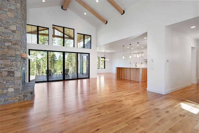 unfurnished living room with light hardwood / wood-style floors, high vaulted ceiling, beamed ceiling, and a stone fireplace