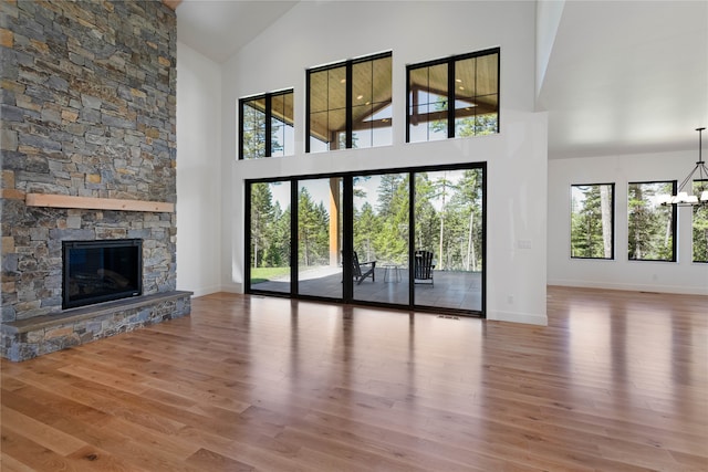 unfurnished living room with a chandelier, a stone fireplace, wood-type flooring, and high vaulted ceiling