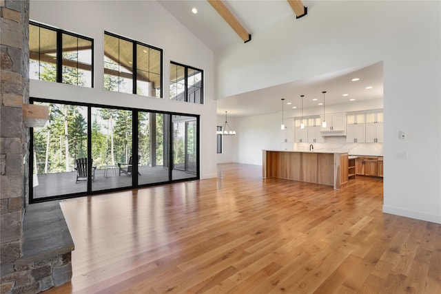 unfurnished living room with light hardwood / wood-style floors, an inviting chandelier, high vaulted ceiling, and beamed ceiling