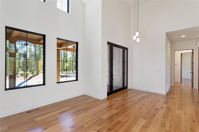 spare room featuring french doors, a towering ceiling, and light wood-type flooring