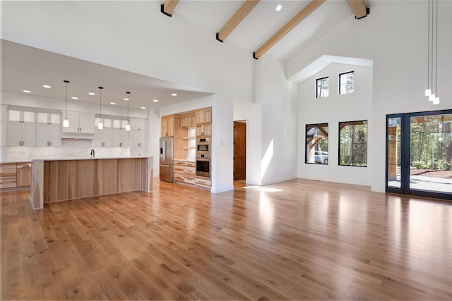 unfurnished living room with beam ceiling, sink, light hardwood / wood-style flooring, and high vaulted ceiling