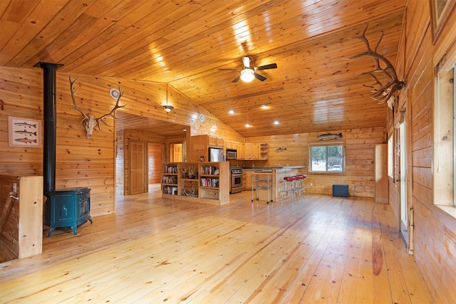 unfurnished living room featuring lofted ceiling, wood ceiling, a wood stove, light wood-type flooring, and wood walls