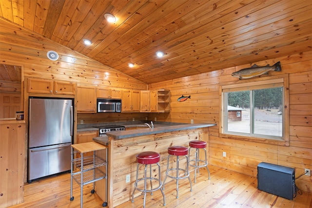 kitchen with lofted ceiling, a breakfast bar area, appliances with stainless steel finishes, wood walls, and light hardwood / wood-style floors