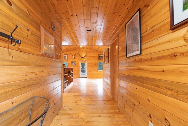 hall featuring light wood-type flooring, wood ceiling, and wooden walls