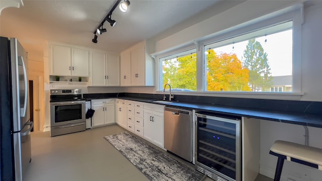 kitchen with sink, white cabinets, rail lighting, beverage cooler, and appliances with stainless steel finishes