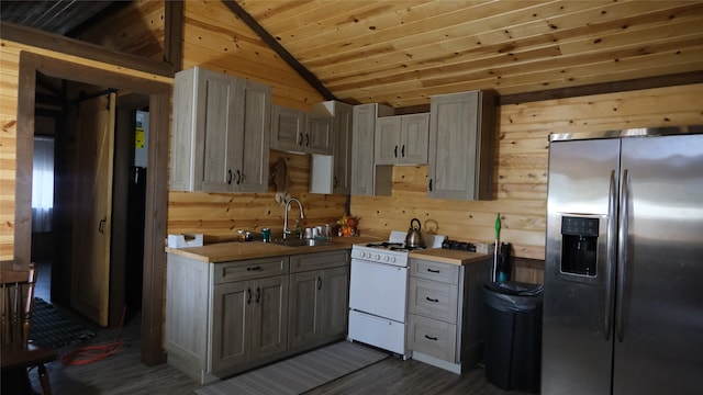 kitchen with stainless steel fridge, vaulted ceiling, sink, white range with gas stovetop, and wooden walls