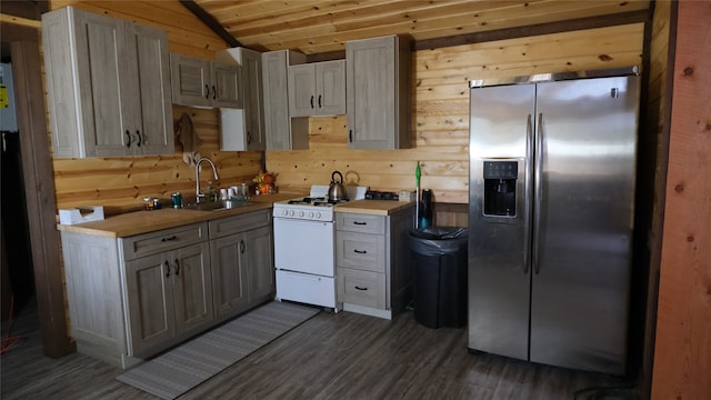 kitchen with wood walls, dark wood-type flooring, white range with gas stovetop, stainless steel refrigerator with ice dispenser, and sink