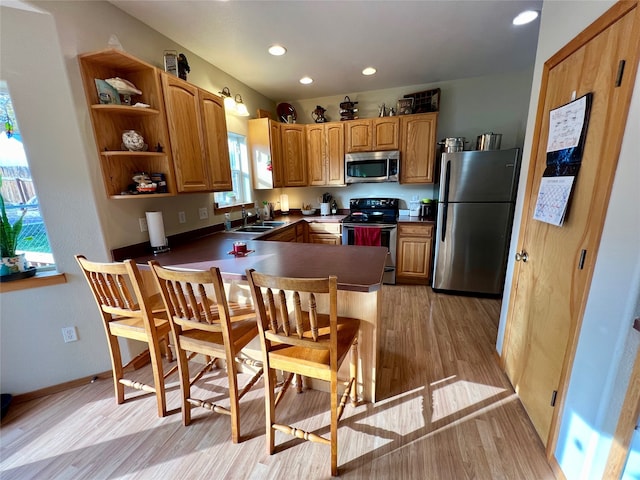 kitchen with light hardwood / wood-style floors, kitchen peninsula, stainless steel appliances, and sink