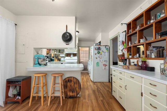 kitchen with kitchen peninsula, hardwood / wood-style floors, electric panel, a breakfast bar, and white appliances