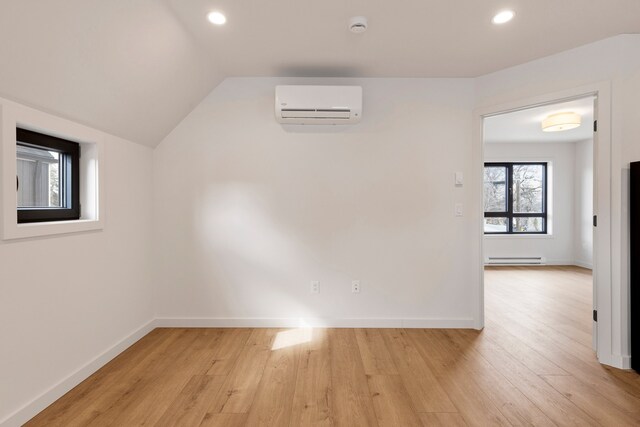 empty room featuring vaulted ceiling, a wall mounted AC, light hardwood / wood-style flooring, and a baseboard heating unit