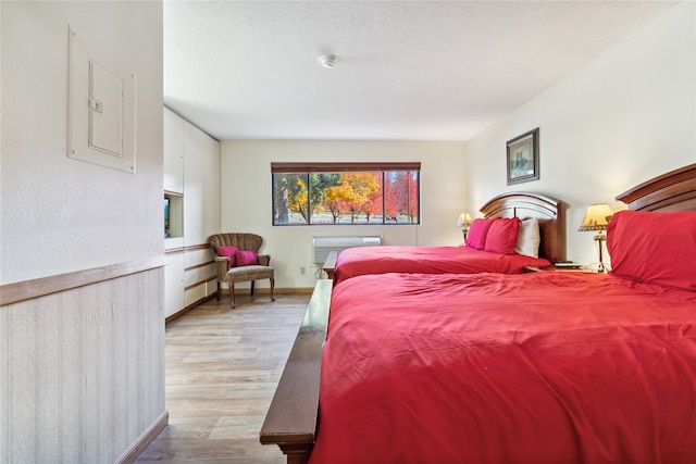 bedroom featuring light hardwood / wood-style floors, electric panel, and a wall mounted air conditioner