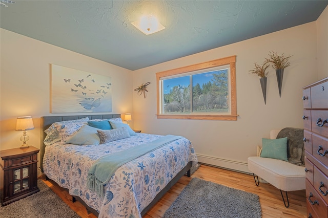 bedroom with hardwood / wood-style floors and a baseboard heating unit