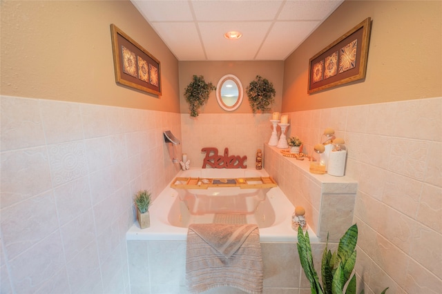 bathroom with a drop ceiling, tiled tub, and tile walls