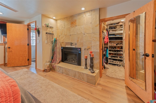 bedroom with a fireplace, a walk in closet, light hardwood / wood-style floors, and ceiling fan