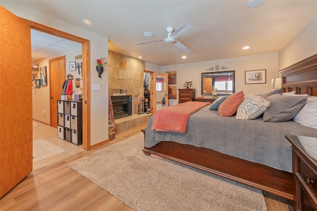 bedroom with a tiled fireplace, light wood-type flooring, and ceiling fan