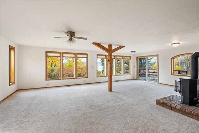 unfurnished living room featuring a wood stove, light colored carpet, a textured ceiling, and ceiling fan