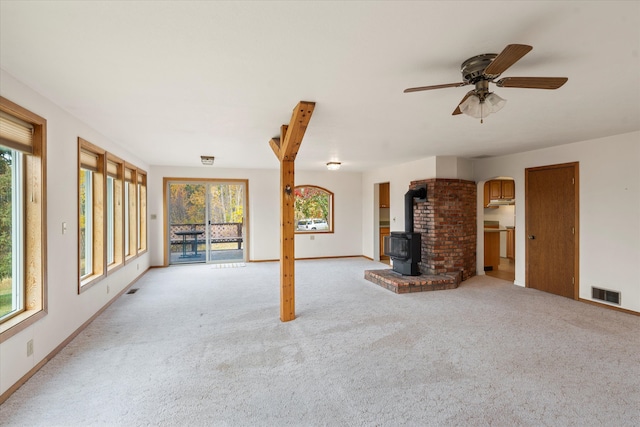 unfurnished living room with a wood stove, a wealth of natural light, and light colored carpet