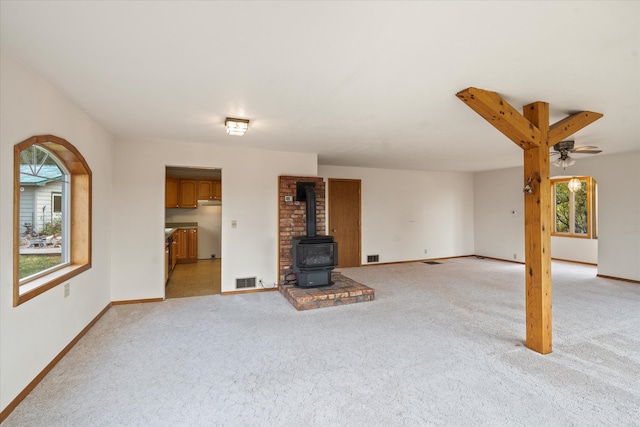 unfurnished living room featuring a wood stove, light carpet, and plenty of natural light