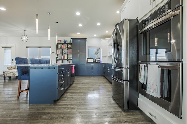 kitchen featuring hanging light fixtures, stainless steel appliances, a center island with sink, a breakfast bar, and white cabinetry