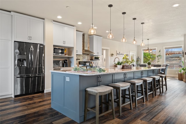 kitchen featuring a large island, white cabinets, stainless steel appliances, wall chimney exhaust hood, and decorative light fixtures