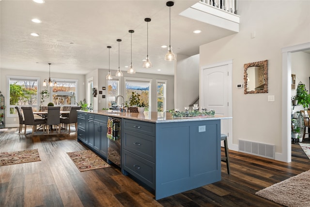 kitchen featuring a center island with sink, decorative light fixtures, dark hardwood / wood-style flooring, and plenty of natural light