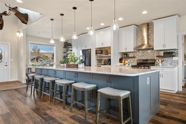 kitchen with wall chimney exhaust hood, a large island with sink, appliances with stainless steel finishes, and white cabinetry