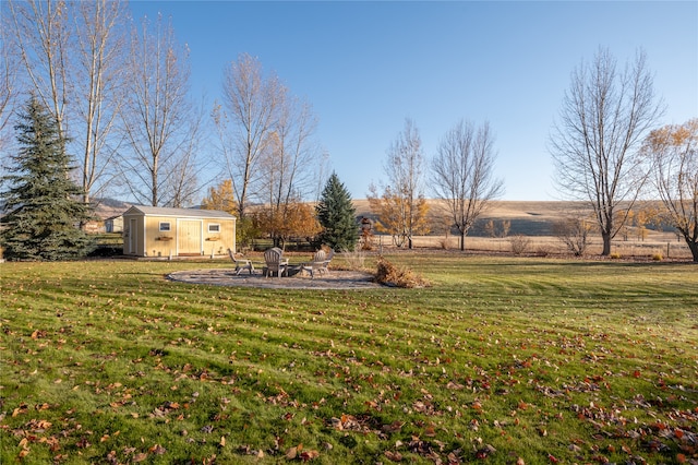 view of yard featuring a patio, an outdoor structure, a fire pit, and a rural view