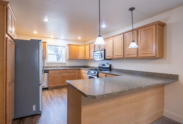 kitchen with kitchen peninsula, appliances with stainless steel finishes, sink, decorative light fixtures, and hardwood / wood-style floors