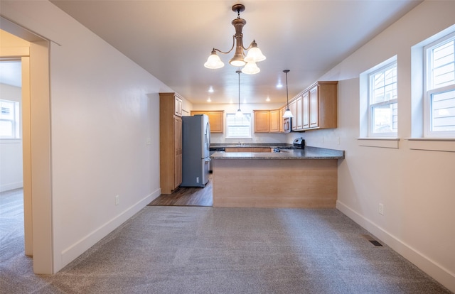 kitchen with light brown cabinets, kitchen peninsula, plenty of natural light, decorative light fixtures, and appliances with stainless steel finishes