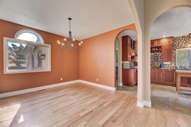 unfurnished dining area featuring an inviting chandelier, light hardwood / wood-style flooring, a textured ceiling, and plenty of natural light