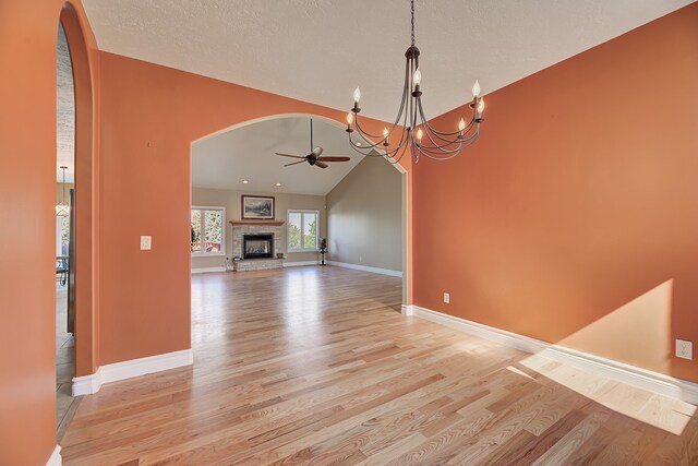 unfurnished dining area with ceiling fan with notable chandelier, a fireplace, a textured ceiling, lofted ceiling, and light hardwood / wood-style flooring