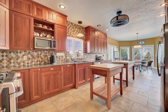 kitchen with hanging light fixtures, stainless steel appliances, sink, light stone countertops, and tasteful backsplash