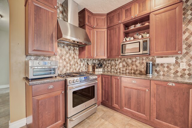 kitchen with wall chimney range hood, tasteful backsplash, appliances with stainless steel finishes, a textured ceiling, and light stone countertops