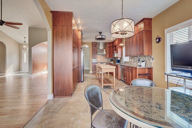 kitchen featuring backsplash, light hardwood / wood-style floors, stainless steel appliances, ceiling fan, and pendant lighting