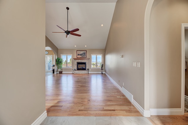 unfurnished living room with a stone fireplace, high vaulted ceiling, light wood-type flooring, and ceiling fan