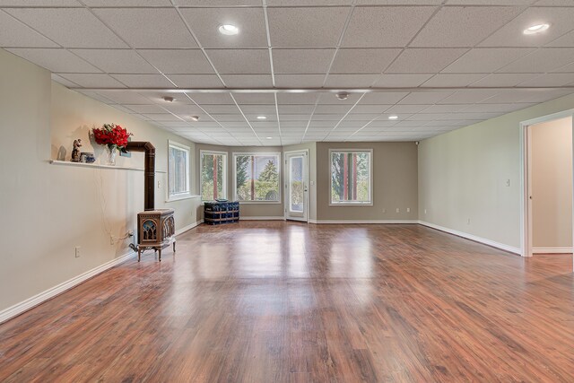 unfurnished room with a drop ceiling, a wood stove, and hardwood / wood-style flooring