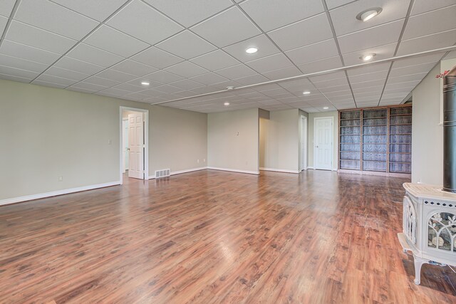 unfurnished living room featuring a drop ceiling, a wood stove, and hardwood / wood-style floors