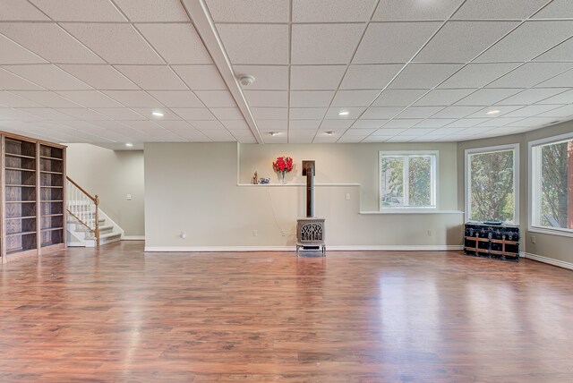 unfurnished living room featuring hardwood / wood-style flooring, a wood stove, and a drop ceiling