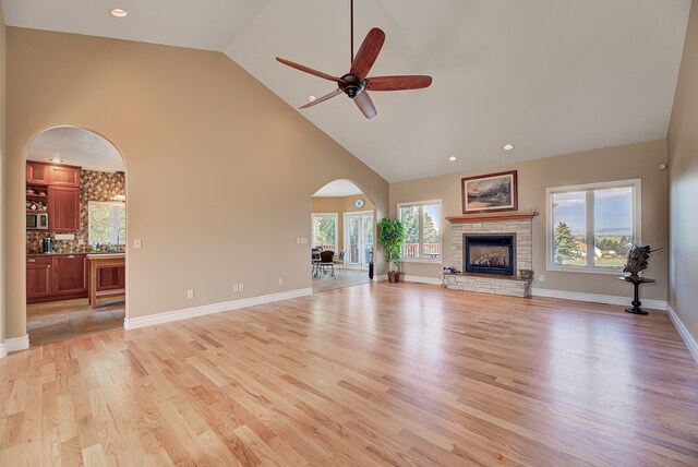 unfurnished living room with a stone fireplace, high vaulted ceiling, light hardwood / wood-style floors, and ceiling fan