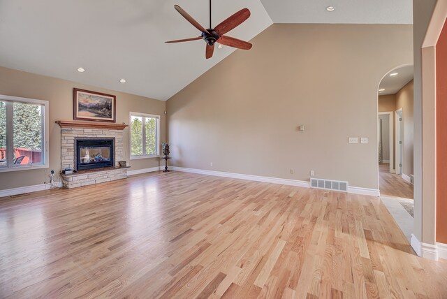 unfurnished living room with light hardwood / wood-style floors, a stone fireplace, high vaulted ceiling, and ceiling fan