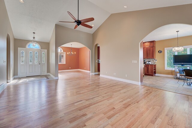 unfurnished living room featuring high vaulted ceiling, ceiling fan with notable chandelier, and light wood-type flooring