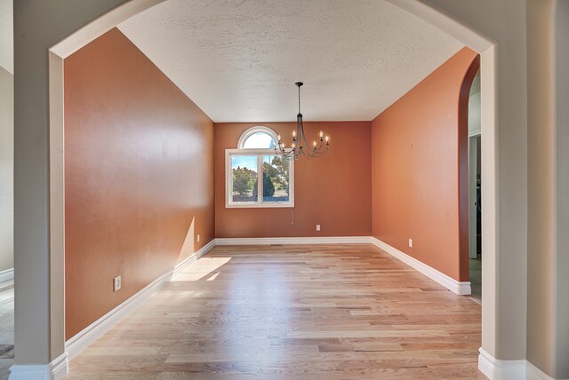 unfurnished dining area featuring an inviting chandelier, light hardwood / wood-style flooring, and a textured ceiling