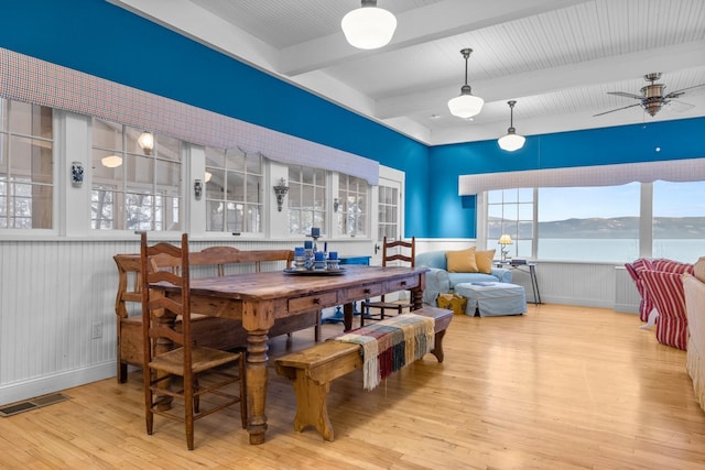 dining room with beam ceiling, light wood-type flooring, ceiling fan, and a water view