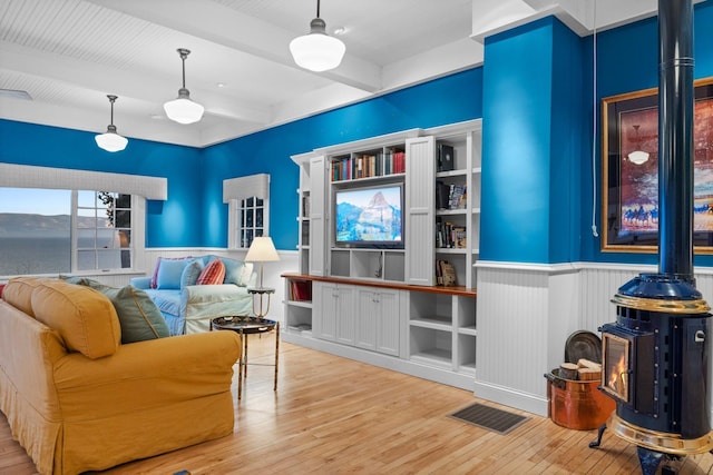 living room featuring light hardwood / wood-style flooring, a water view, beamed ceiling, and a wood stove