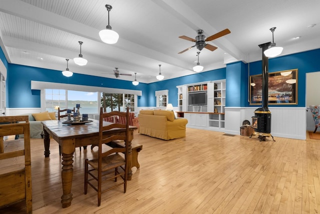 381 Lakeside Blvd, Lakeside, MT 59922 - dining space with a ceiling fan, beamed ceiling, a wood stove, hardwood / wood-style flooring, and a wainscoted wall