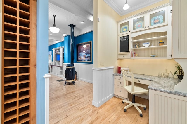 office area with built in desk, light hardwood / wood-style flooring, a wood stove, ornamental molding, and beamed ceiling