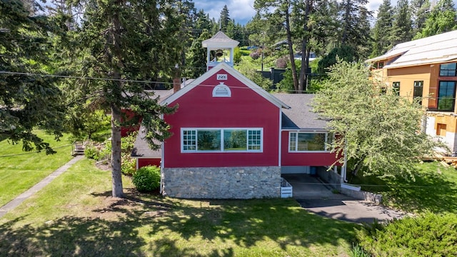 381 Lakeside Blvd, Lakeside, MT 59922 - view of front facade featuring a front lawn, a shingled roof, stone siding, and view of wooded area